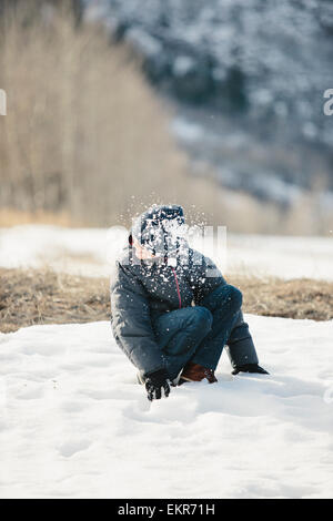 Un ragazzo in un mantello blu e cappellino girando la testa da una palla di neve che ha colpito. Foto Stock