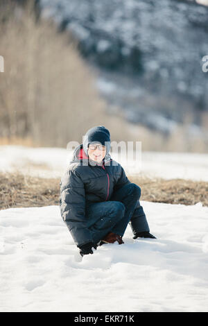 Un ragazzo in un mantello blu e cappellino nella neve. Foto Stock