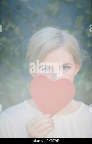 Donna che mantiene un cuore rosso forma nella parte anteriore del suo volto. Foto Stock