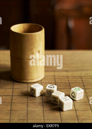 Cinque dadi con facce stampato su un pub in legno tavolo e una coppa di legno accanto a loro. Foto Stock