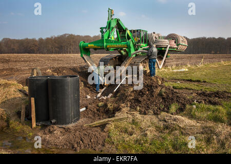 I collaboratori che lavorano con il drenaggio scavatrincee / tile aratro su terreno coltivato Foto Stock