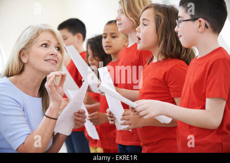 I bambini nel canto del gruppo essendo incoraggiati dall'insegnante Foto Stock