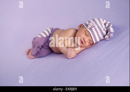 Sorridente otto giorni di età neonato ragazza dorme pacificamente su un sfondo lilla. Foto Stock