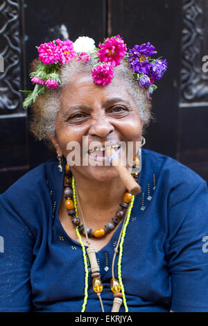 Una donna anziana con fiori nei capelli di fumare un sigaro in Havana, Cuba Foto Stock