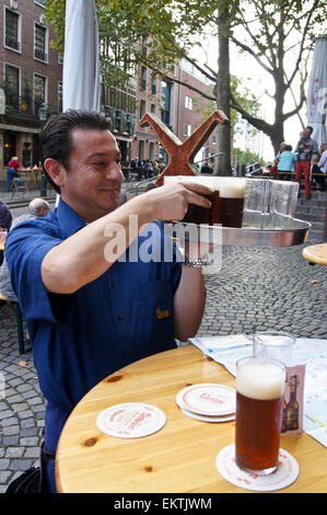 Köbes (barman) servente Altbier a Uerige brauhaus, Düsseldorf, Renania settentrionale-Vestfalia, Germania pub tavola bicchieri di bevande Foto Stock