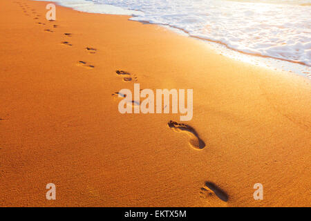 Spiaggia, onde e impronte in tempo al tramonto Foto Stock