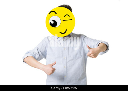 Giovane uomo dando pollice in alto con un Winking Emoticon nella faccia anteriore del suo volto Foto Stock