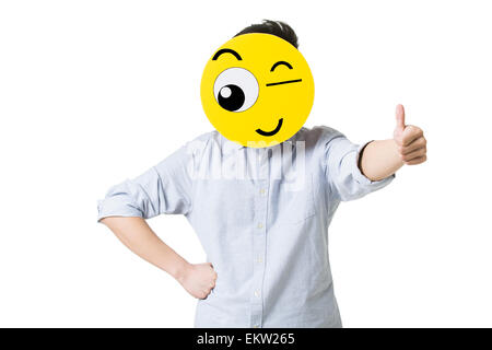 Giovane uomo dando pollice in alto con un Winking Emoticon nella faccia anteriore del suo volto Foto Stock