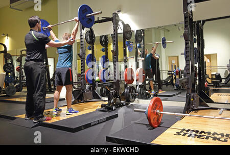 Il peso della formazione in un moderno Londra centro fitness. Un maschio di istruttore sovrintende una palestra gli stati di sollevamento pesi tradizionali Foto Stock