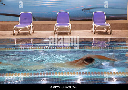 Lane di nuoto in una privata a Londra la piscina nel seminterrato. Mostra un nuotatore non identificabili passando sedie a sdraio vuota. Crawl anteriore corsa. Foto Stock