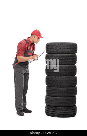 A piena lunghezza Ritratto di una giovane meccanico di controllo della qualità di un set di pneumatici e di scrivere le note su un clipboard Foto Stock