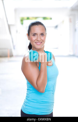 Bella donna sportiva nella formazione blu bicipite con manubrio blu all'aperto Foto Stock
