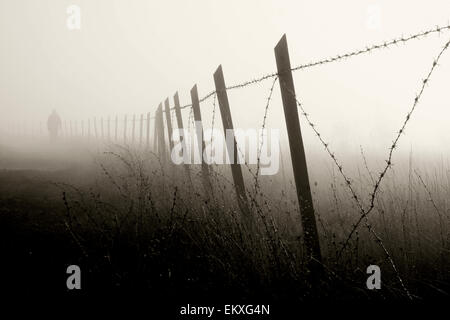 Uomo che cammina vicino al recinto di filo spinato nella fitta nebbia Foto Stock