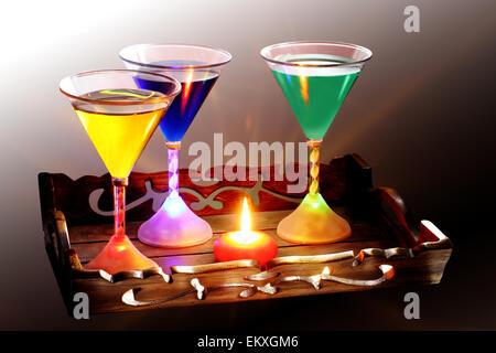 Un vassoio decorato intagliato che contiene una candela e tre bicchieri da cocktail, ogni vetro è illuminato dall'interno della base da luci a LED Foto Stock