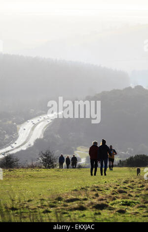 La gente che camminava sul sud giù a Butser hill in silhouette con A3 trunk road Foto Stock