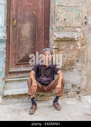 Un cubano ispanico uomo si siede sul chinarsi davanti a casa sua con parete di frantumazione nella Habana Vieja, Cuba. Foto Stock