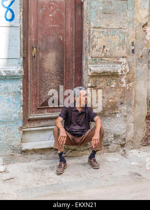 Un cubano ispanico uomo si siede sul chinarsi davanti a casa sua con parete di frantumazione nella Habana Vieja, Cuba. Foto Stock