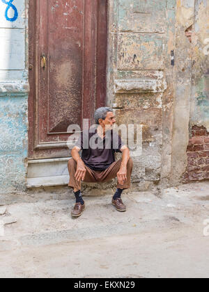 Un cubano ispanico uomo si siede sul chinarsi davanti a casa sua con parete di frantumazione nella Habana Vieja, Cuba. Foto Stock