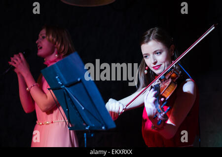 Un concerto di tre donna (ragazze) in rosa e rosso abiti a Minsk Loft Club, due violini + cantante Foto Stock