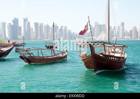 In legno tradizionali barche Dhow ormeggiati sul bordo di un pontile, con lo skyline della città di Doha in background. Il Qatar. Foto Stock