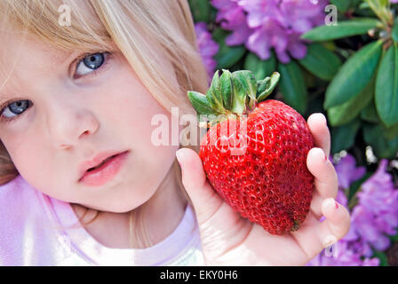 Bimba bionda in un giardino di rododendro con una grande fragola. Foto Stock