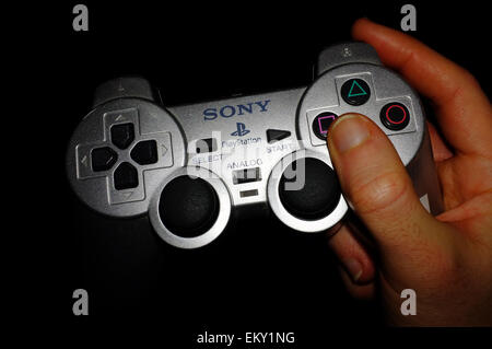 Una mano che tiene un argento Playstation controller con uno sfondo nero. Foto Stock