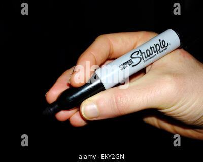 Una mano bianca tenendo un pennarello indelebile Sharpie pen contro uno sfondo nero. Foto Stock