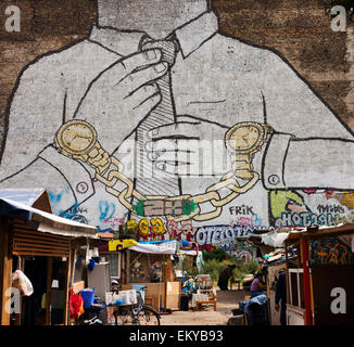 Murale di blu in Berlino Kreuzberg con un campo di sfollati Roma persone sul terreno vacante nella parte anteriore. Foto Stock
