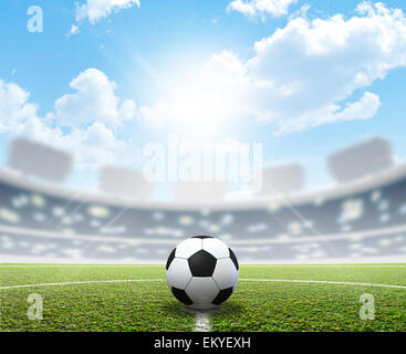 Uno stadio di calcio con una marcata erba verde passo e un pallone da calcio nel centro di giorno sotto un cielo blu Foto Stock