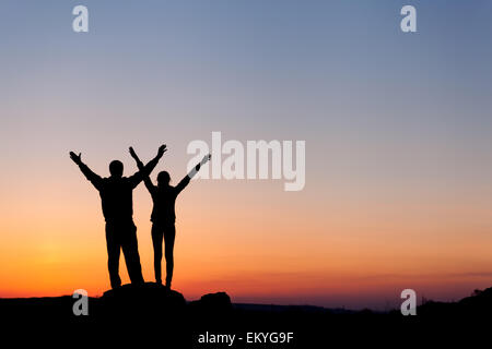 Silhouette di felicità famiglia con bracci sollevati fino contro il bellissimo cielo colorati. Tramonto d'estate. Paesaggio Foto Stock