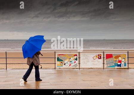 Una persona che cammina con un ombrellone in una passeggiata lungo l'acqua in un giorno di pioggia; Redcar, Teesside, Inghilterra Foto Stock