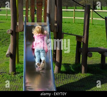 Un bambino di 2 anni toddler girl ritornando indietro verso il basso un parco slitta Inghilterra,UK Foto Stock