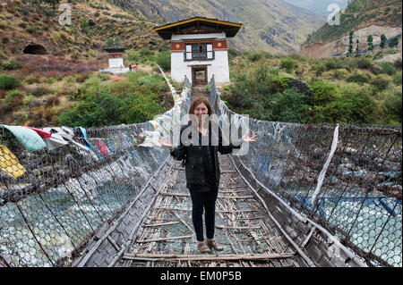 Una donna si erge su un ferro ponte di sospensione rivestiti con bandiere di preghiera; Tamchhog Lhakhang Bhutan Foto Stock