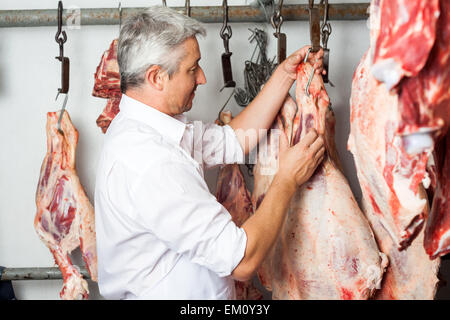 Butcher appendere la carne rossa nel macello Foto Stock