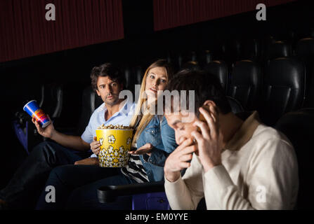 Arrabbiato giovane guardando l'uomo utilizzando mobilephone in teatro Foto Stock