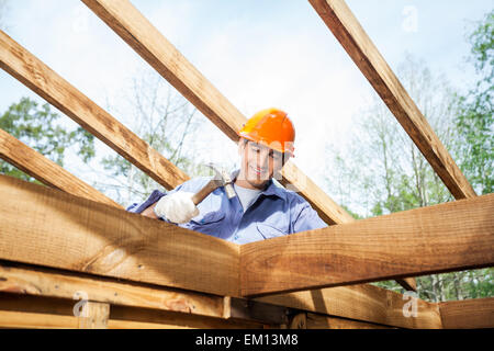 Lavoratore chiodo di martellamento su incompleta cabina in legno presso il sito Foto Stock