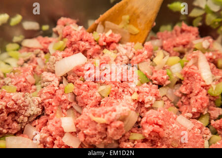 Cucinare la carne macinata, la cipolla tritata e il sedano in una padella con il cucchiaio di legno Foto Stock