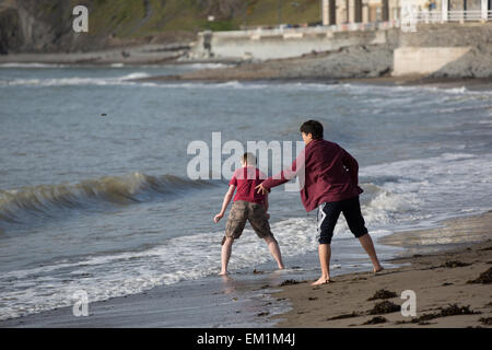 Aberystwyth, Wales, Regno Unito. Il 15 aprile 2015. Meteo. I giovani la scrematura di pietre sulle onde del sole Credito: Alan Hale/Alamy Live News Foto Stock
