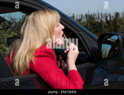 Automobilista femmina applicando lip gloss utilizzando la guida specchietto laterale Foto Stock