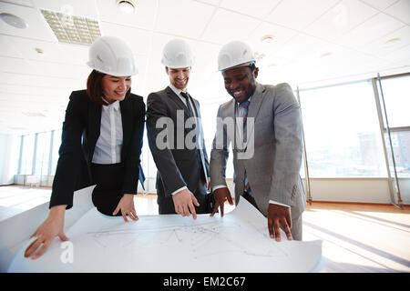 Certi architetti in caschi protettivi guardando il blueprint Foto Stock