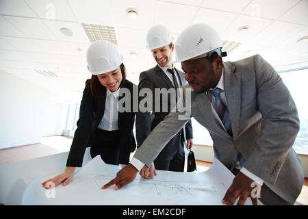 Certi architetti in caschi protettivi guardando il blueprint Foto Stock