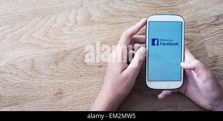 Mani tenendo il telefono cellulare con schermo di facebook o del logo Foto Stock