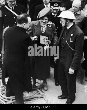 Queen Elizabeth mani una foto delle sue due figlie che ha trovato tra i detriti di un bombardato fuori strada nell'East End, a operai post durante il suo tour della zona seguendo un nazista Air Raid. Guardando indietro è il suo marito King George VI. Il 24 aprile 1941. Foto Stock