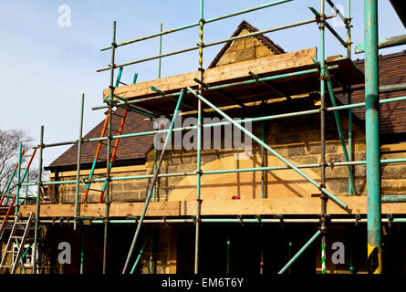 Ponteggio poli accanto al tetto di un edificio sito con nuove tegole del tetto Foto Stock