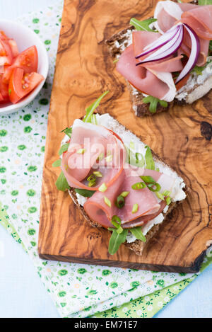 Aprire panini al prosciutto, pomodoro e rucola su olive wood board, vista dall'alto Foto Stock
