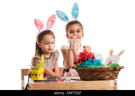 Due bambine nella scuola materna di seduta a tavola e di pittura e decorazione di uova di Pasqua Foto Stock