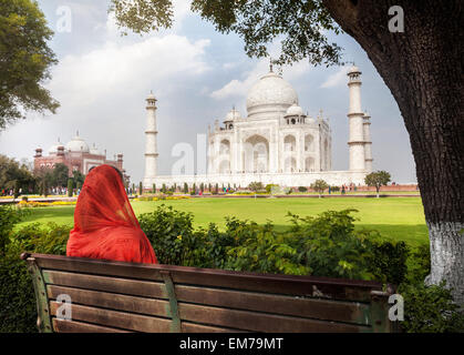 La donna in sciarpa rossa seduta sul banco in ombra e guardando al Taj Mahal di Agra, Uttar Pradesh, India Foto Stock