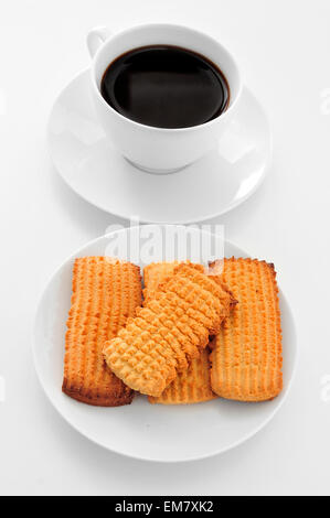 Una tazza di caffè e una piastra con alcuni biscotti su un tavolo bianco Foto Stock
