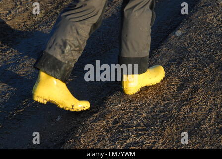 Passeggiata primaverile, camminando su una strada di fango con stivali gialli. Foto Stock