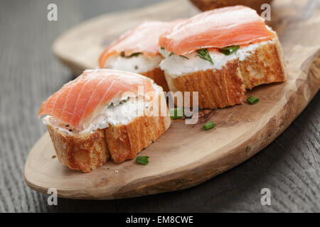 Fette di baguette con salmone affumicato e crema di formaggio su un tavolo di legno Foto Stock